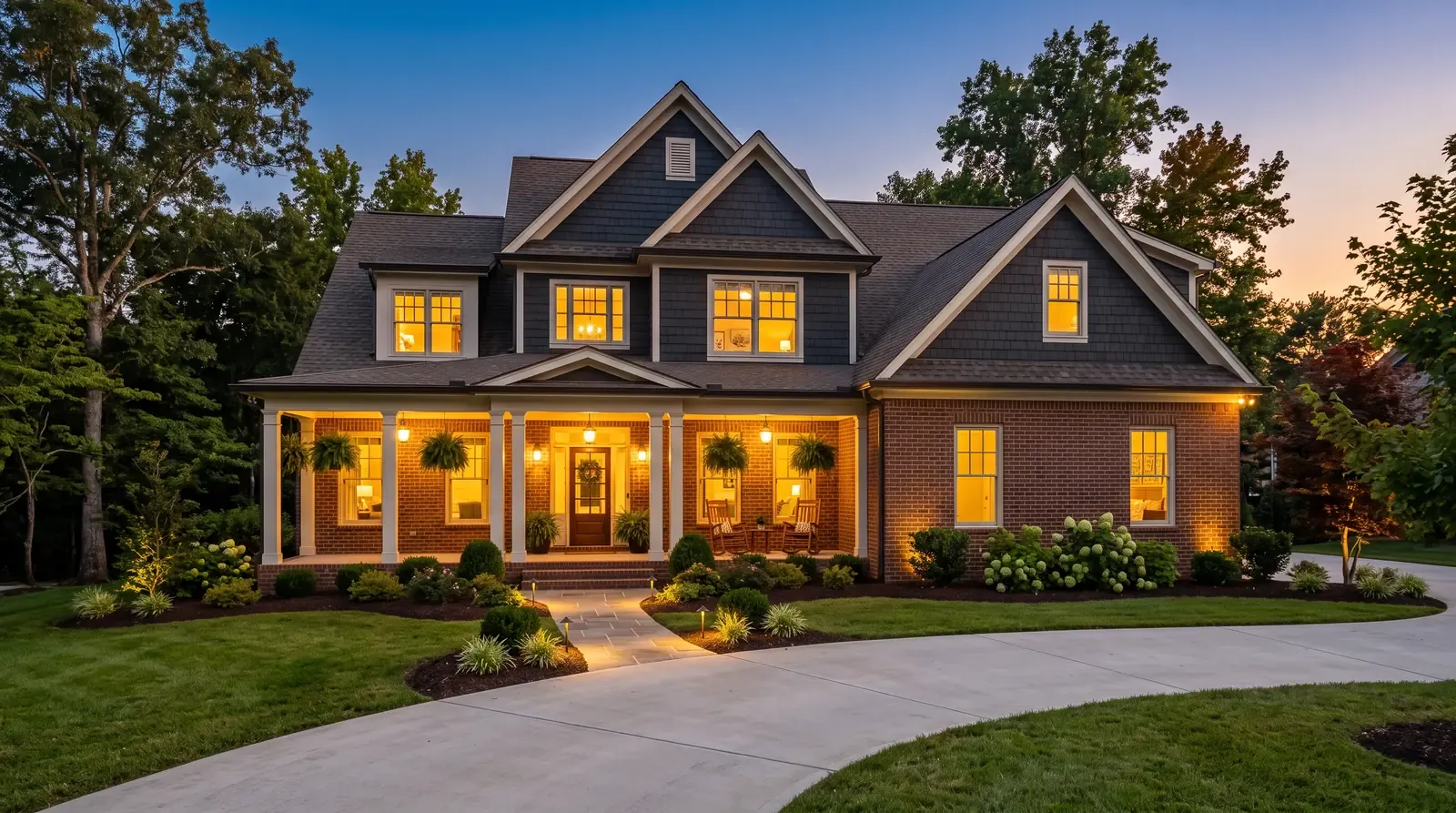 A handsome two-story Tennessee home at dusk with warm light glowing in the windows, a tidy porch and landscaping and a clean driveway