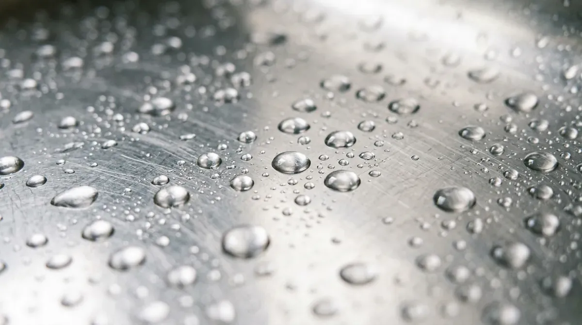 A macro shot of water droplets on a polished stainless steel sink surface, soft light