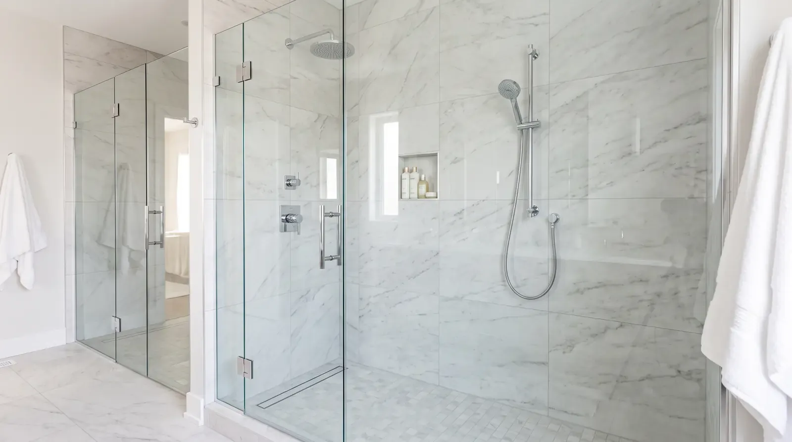 A frameless glass walk-in shower with a rain shower head and a handheld wand, chrome fixtures and large format tile walls