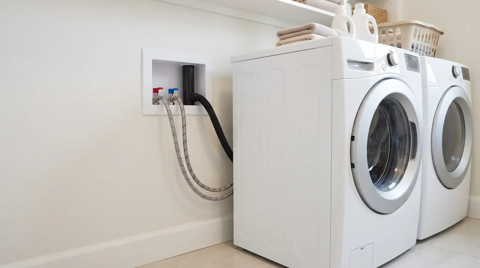 A bright laundry room with a front-load washer and a recessed wall box with hot and cold shutoff valves and a drain standpipe