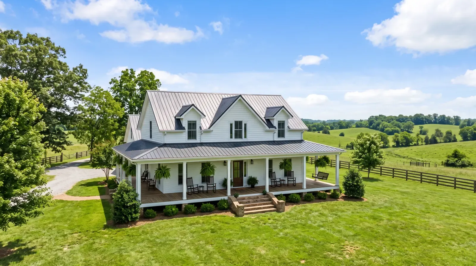 A white farmhouse-style country home in rural Middle Tennessee with a wide covered porch, rocking chairs and rolling green hills behind it